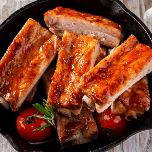 oven baked pork ribs served in a skillet with some veggies.
