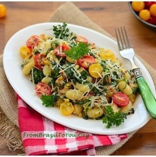Gnocchi com Couve, Toucinho, Milho, e Tomate em um prato branco com um garfo verde