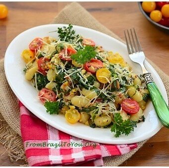 Gnocchi com Couve, Toucinho, Milho, e Tomate em um prato branco com um garfo verde