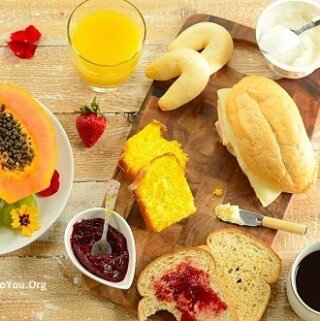 Brazilian breakfast board with sliced papaya, tapioca rolls, bliced bread, orange juice, and sliced papaya