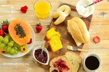 Brazilian breakfast board with sliced papaya, tapioca rolls, bliced bread, orange juice, and sliced papaya