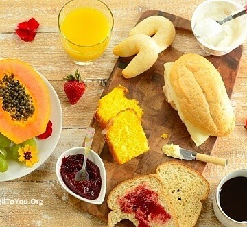Brazilian breakfast board with sliced papaya, tapioca rolls, bliced bread, orange juice, and sliced papaya