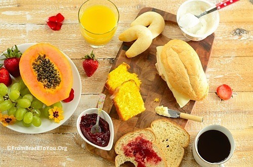 Brazilian breakfast board with sliced papaya, tapioca rolls, bliced bread, orange juice, and sliced papaya