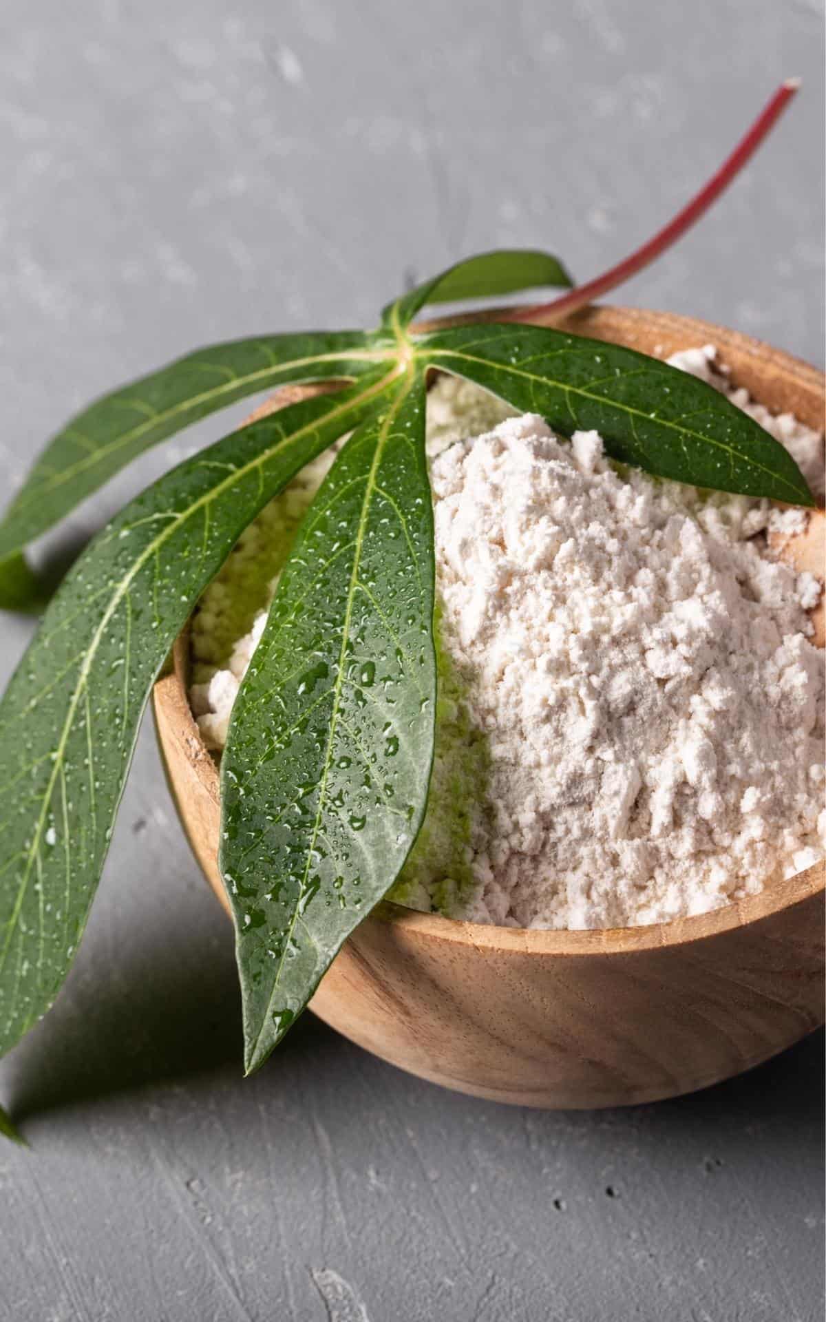 a bowl of cassava flour with adn cassava leaves on top