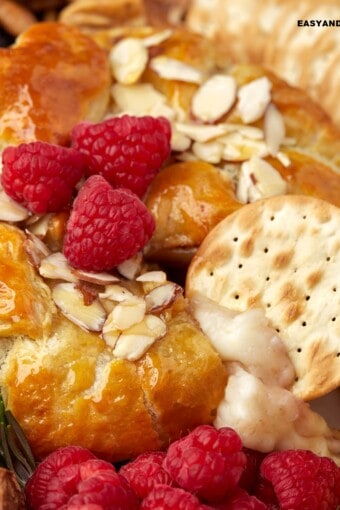 close up of a cracker dipped in baked brie en croute with jam and honey.