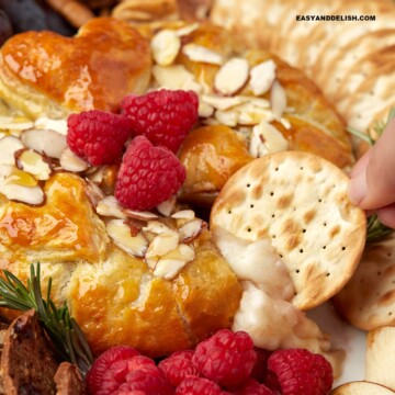 close up of a cracker dipped in baked brie en croute with jam and honey.