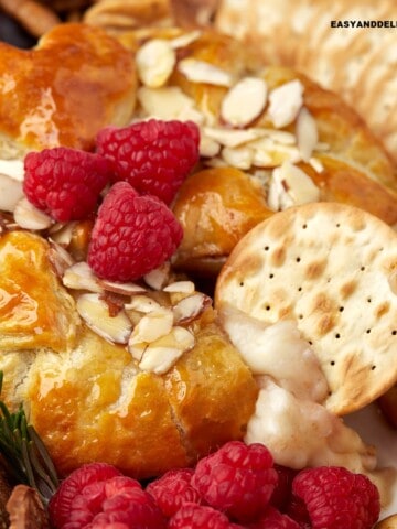 close up of a cracker dipped in baked brie en croute with jam and honey.