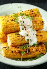 a pile of grilled corn on the cob with sauce on top