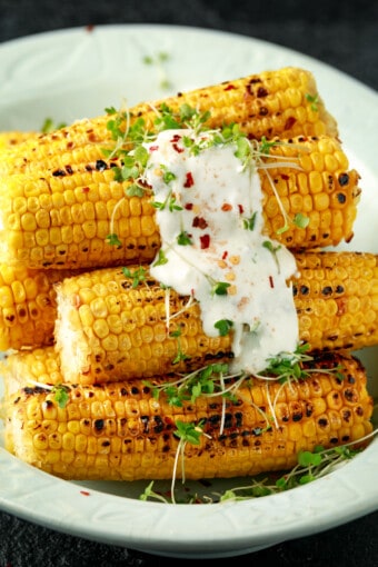 a pile of grilled corn on the cob with sauce on top