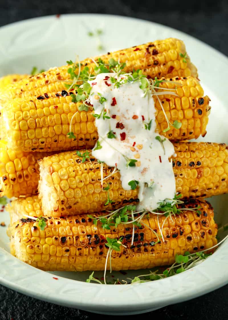 a pile of grilled corn on the cob with sauce on top