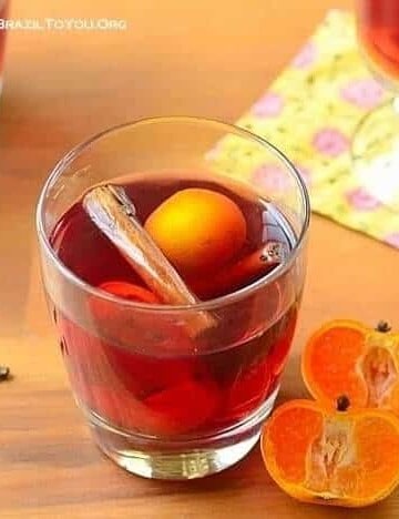 A glass of Brazilian mulled wine with orange halves on the side