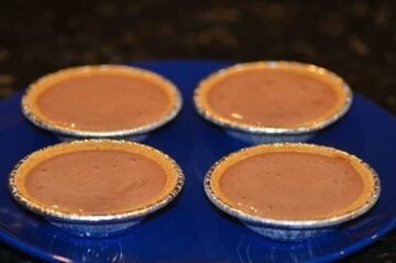 Four mini graham cracker pie crusts on a blue plate which are filled with the chocolate pudding ice cream mixture