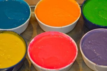 bowls of divided batter colored with several different shades of food coloring