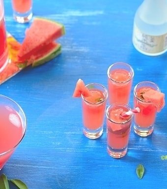 4 glasses of watermelon caipisake on a blue board