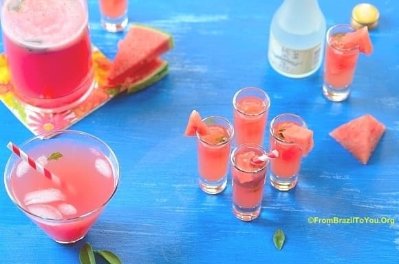 4 glasses of watermelon caipisake on a blue board