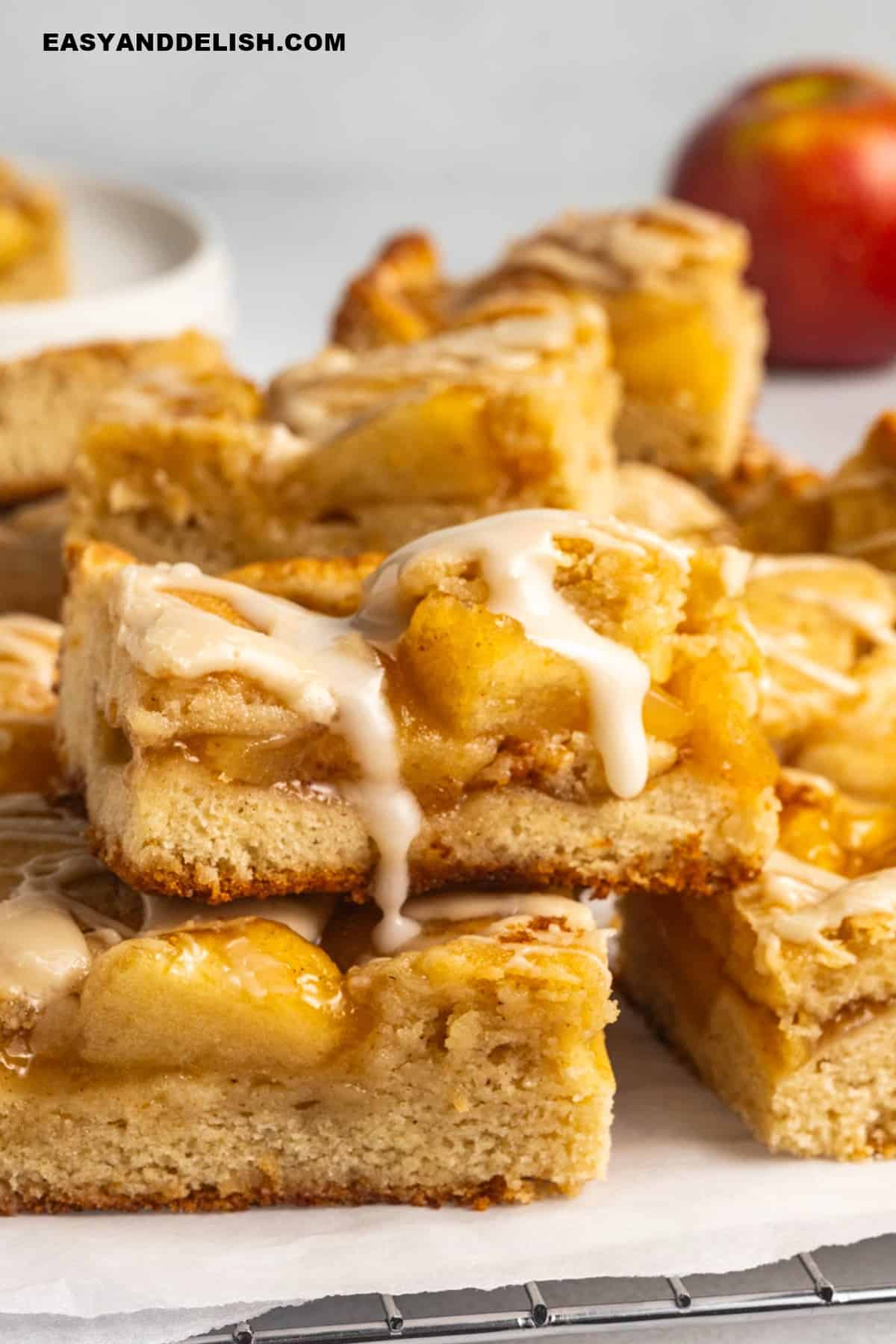 apple pie bars topped with a vanilla glaze dripping down.