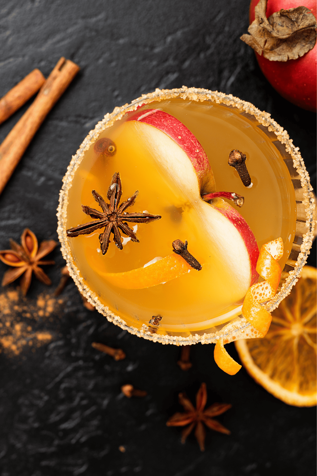 a glass of hot apple cider cocktail with apple and spices in it.