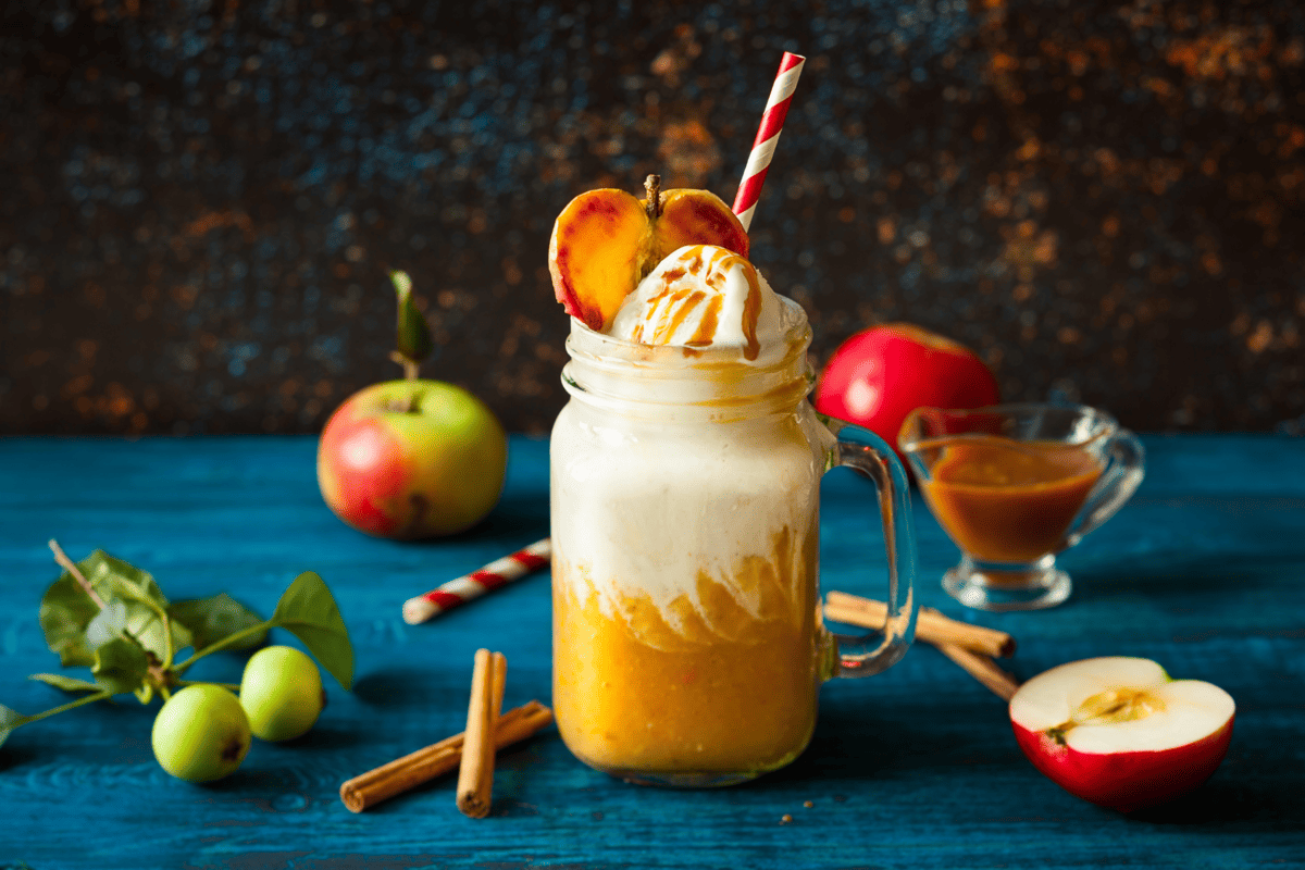 caramel apple cider topped with whipped cream and caramel sauce plus apples.