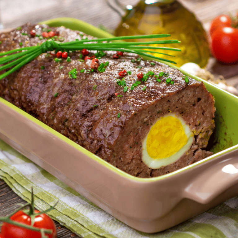 close up of German meatloaf with hard-boiled egg in a baking dish topped with red pepper and chives.
