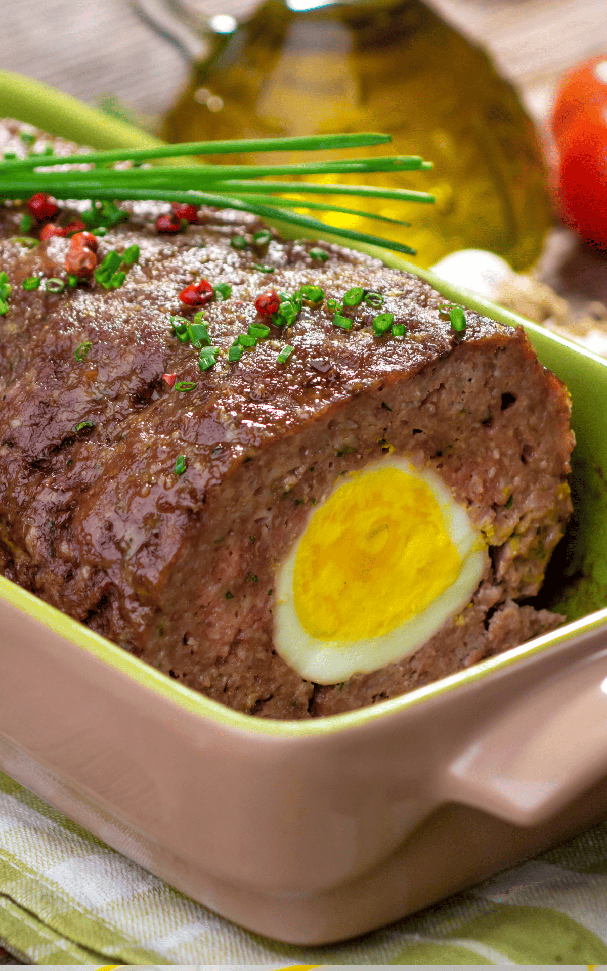 German meatloaf with hard-boiled egg in a baking dish with herbs on top.