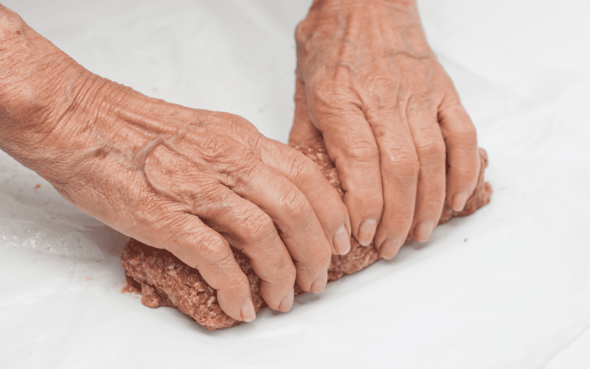 Shaping egg stuffed meatloaf with hands.