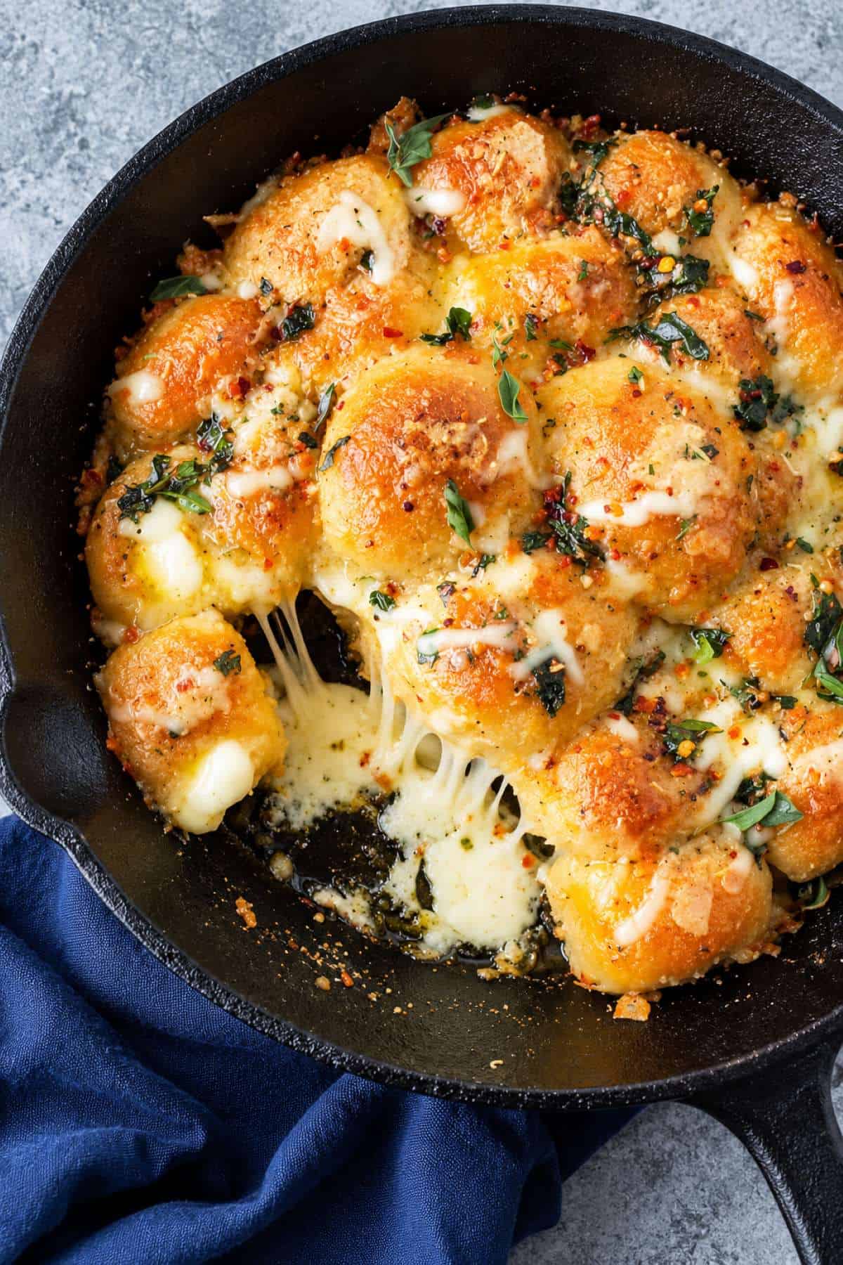Cheese-stuffed garlic bread rolls with melted cheese, garlic butter, and fresh herbs in a cast-iron skillet.