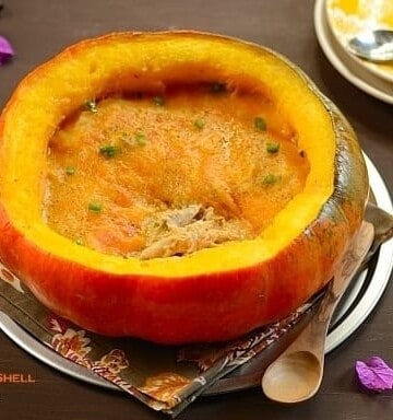 A half pumpkin shell filled with chicken stew topped with melted cheese