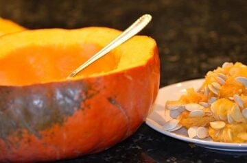 pumpkin seeds being scooped out with a spoon onto a plate