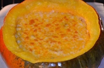 pumpkin shell filled with stew and topped with shredded cheese that has been broiled
