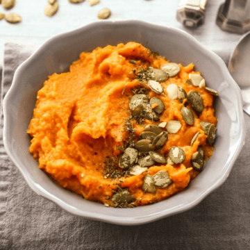 A bowl of savory mashed sweet potatoes with coconut milk, topped with pepitas.