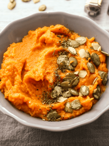A bowl of savory mashed sweet potatoes with coconut milk, topped with pepitas.