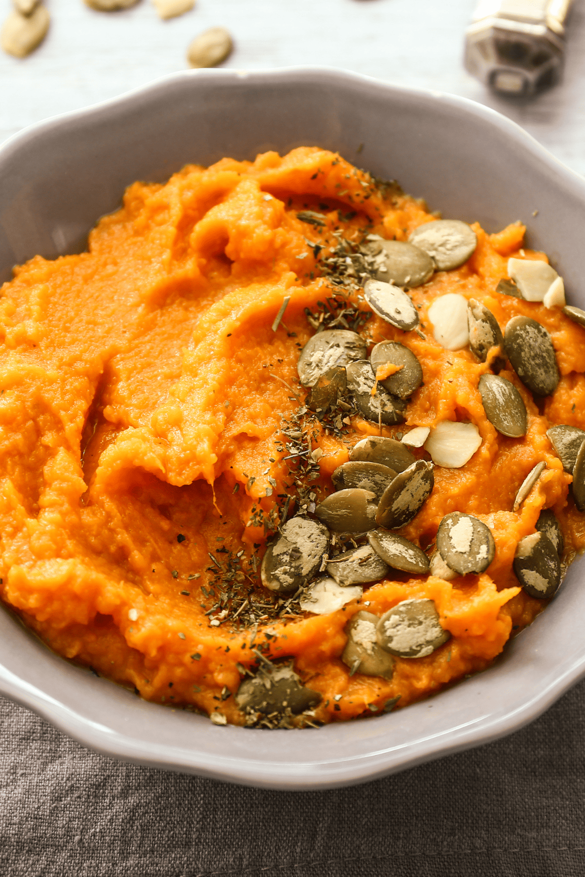 Savory mashed sweet potatoes with coconut milk, served in a bowl with pepitas on top.  