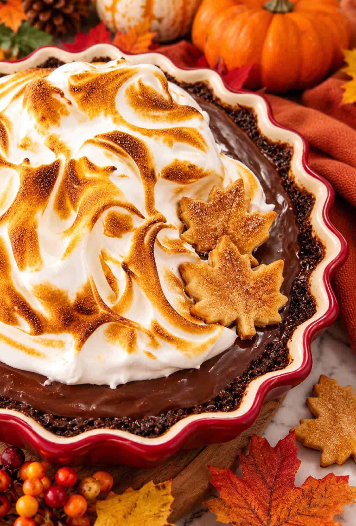 Chocolate pie with toasted meringue, maple leaf cookies, pumpkins, and autumn leaves for Thanksgiving.
