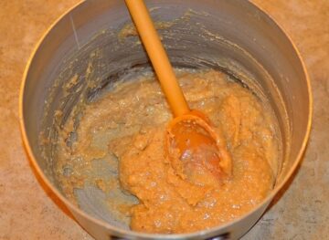 dough being stirred in a metal pot with a wooden spoon
