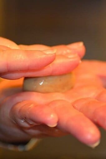 ball of dough being flattened between fingers and the palm of another hand