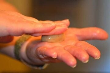 ball of dough being flattened between fingers and the palm of another hand