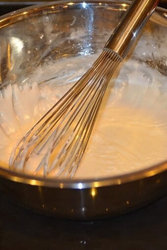 powdered sugar, milk, and lemon juice being whisked in a metal bowl