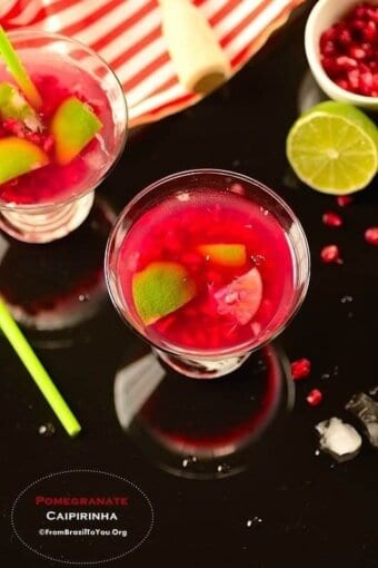 glasses of pomegranate caipirinha on a table with garnishes on the sides