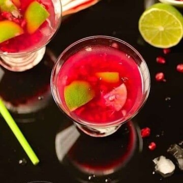 glasses of pomegranate caipirinha on a table with garnishes on the sides