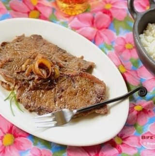 A plate of steak and onions on a plate with a fuschia pink flower pattern tablecloth