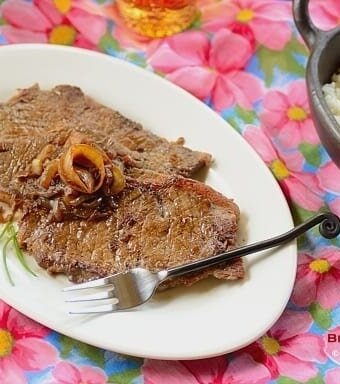 A plate of steak and onions on a plate with a fuschia pink flower pattern tablecloth