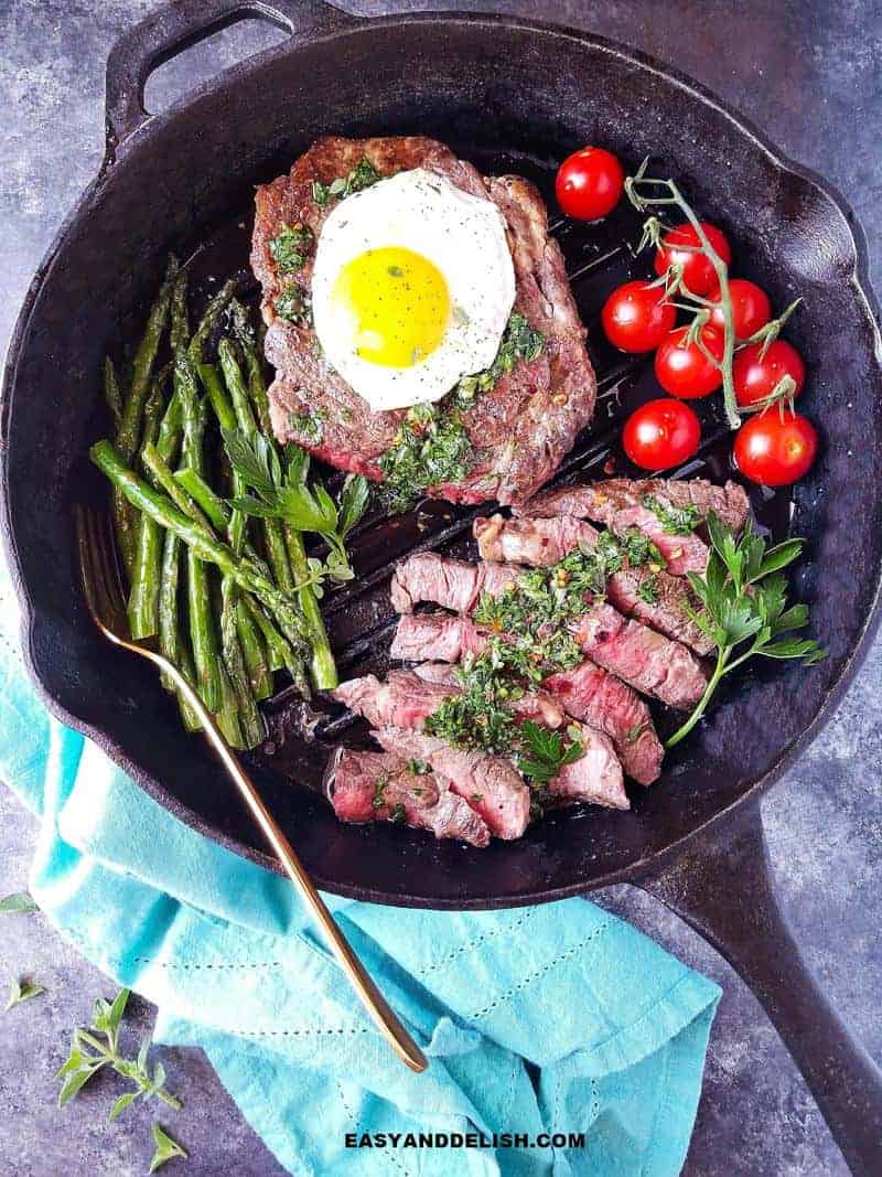 a large skillet with partially sliced steak with an egg on top and veggies on the side