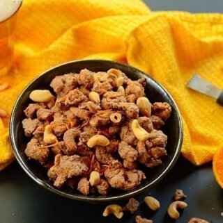 A bowl of glazed cashew nuts with a yellow cloth on the side