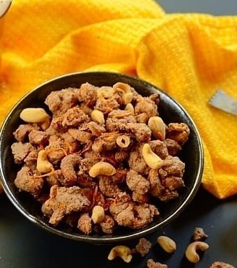 A bowl of glazed cashew nuts with a  yellow cloth on the side