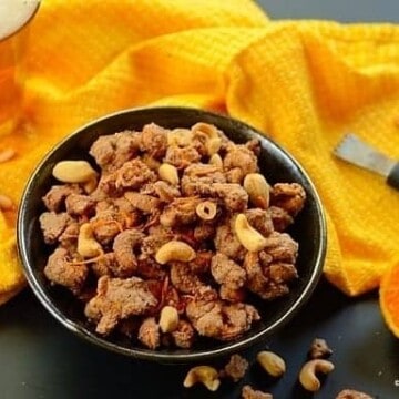 A bowl of glazed cashew nuts with a  yellow cloth on the side