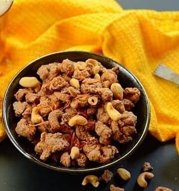 A bowl of glazed cashew nuts with a  yellow cloth on the side