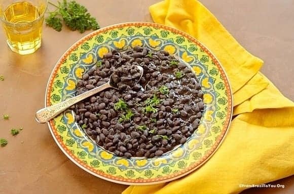 Feijão preto or black beans in a yellow, green, and blue serving bowl 