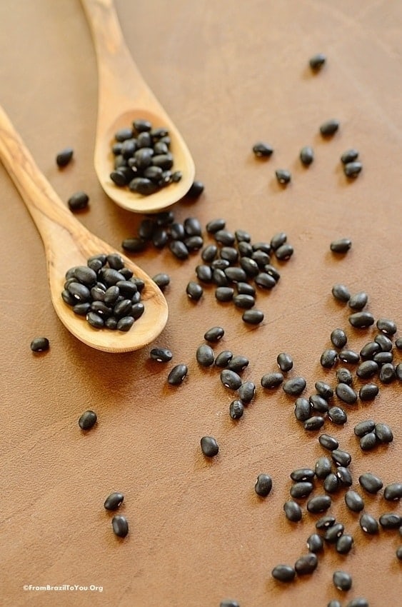 dry black beans over a surface with 2 wooden spoons