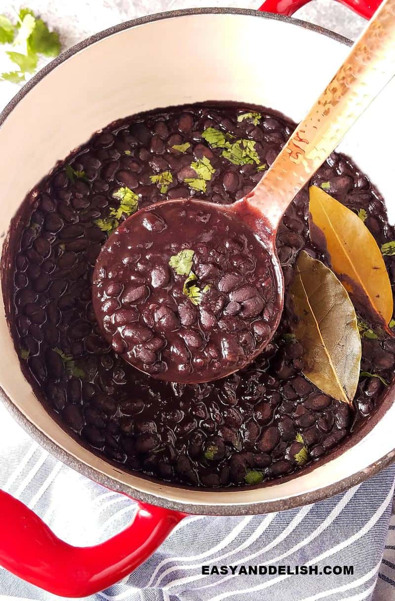 a pot of black beans cooked form scratch with a ladle in the middle