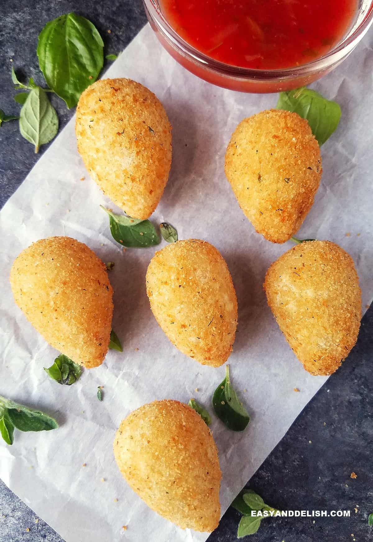 Several chicken croqeuttes spread on a table witha  bowl of sauce on the side.